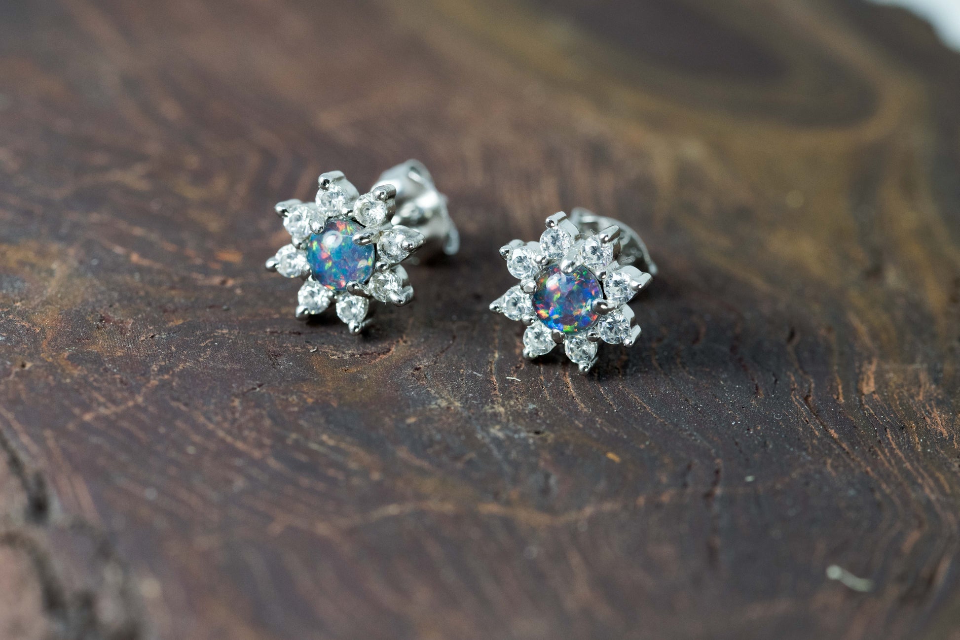 Pair of silver opal earrings with gemstones on a wooden surface