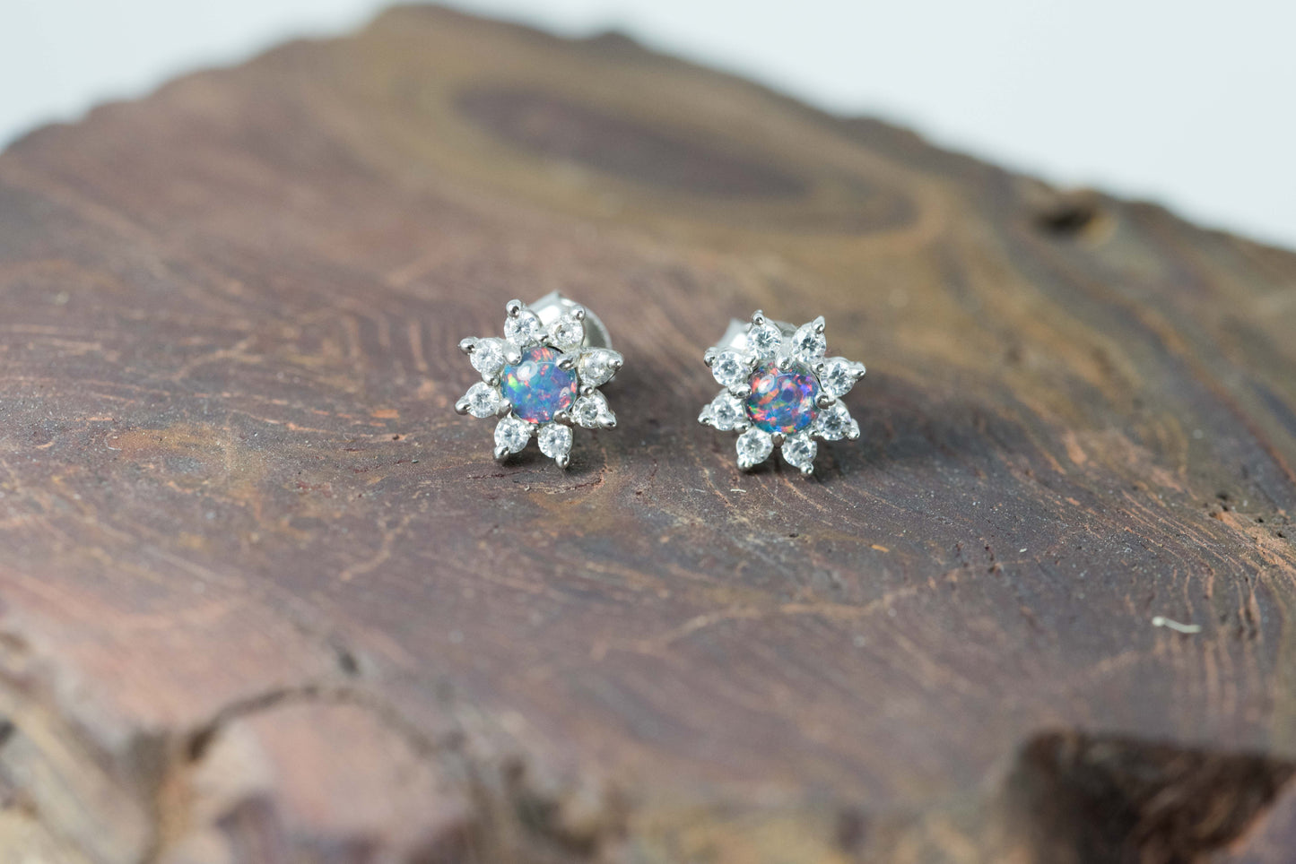 Pair of silver flower-shaped earrings with colorful opal gemstones on a wooden surface