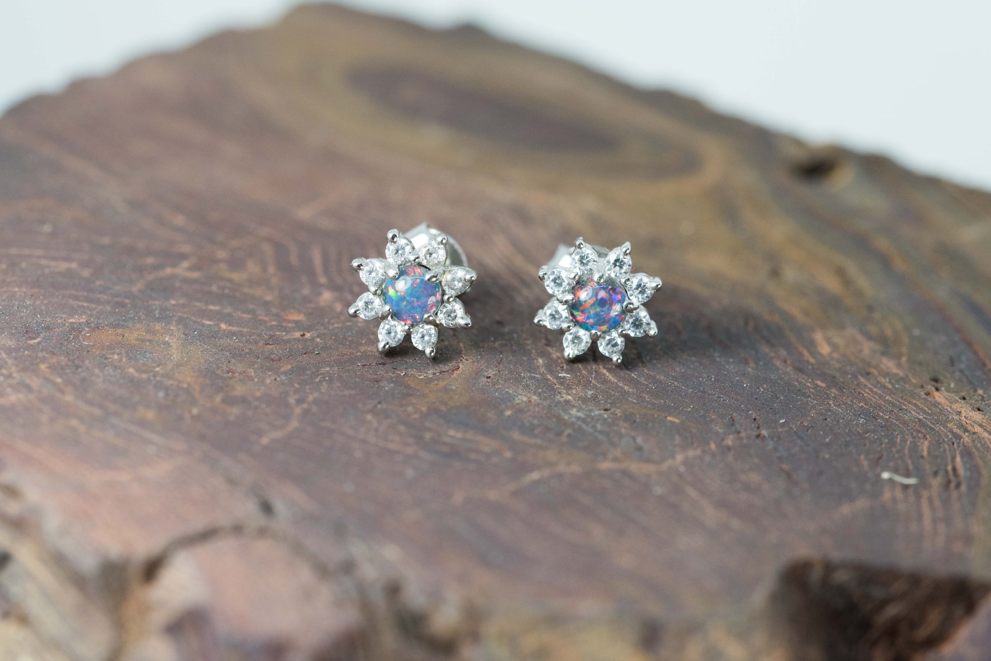 Pair of silver flower-shaped earrings with colorful opal gemstones on a wooden surface