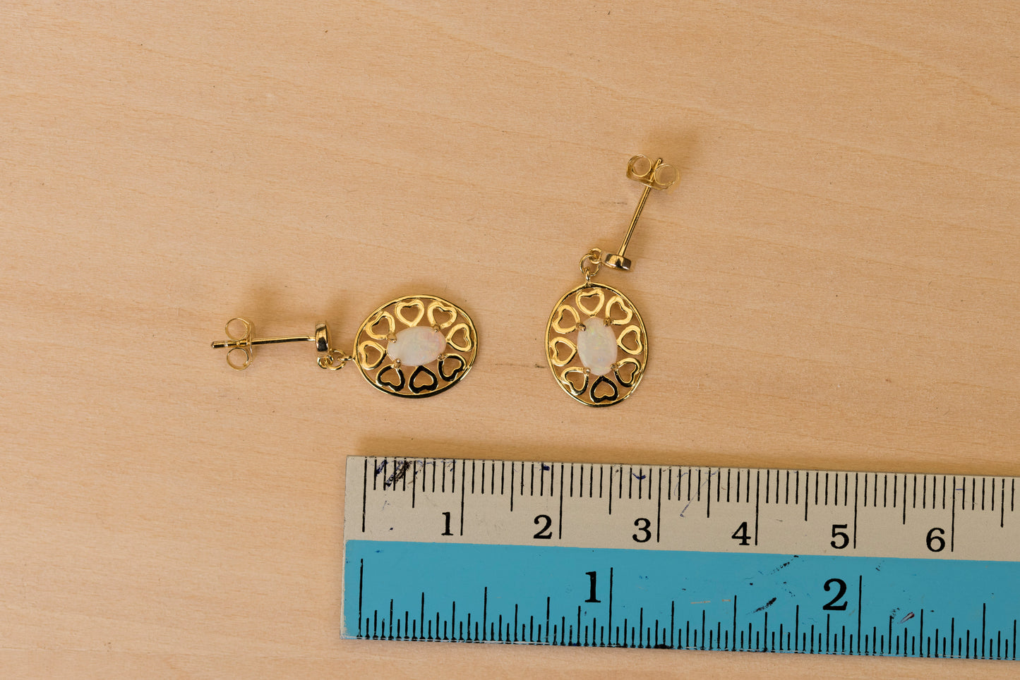 Gold earrings with circular designs on a wooden surface with a ruler for scale.