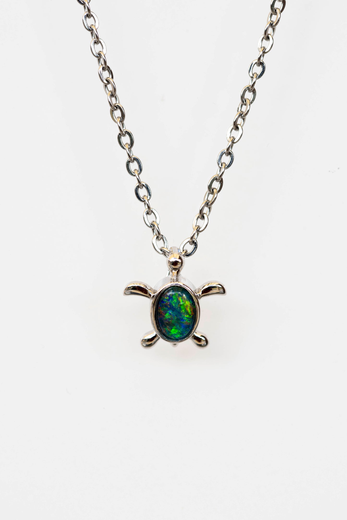 Turtle-shaped pendant necklace with a multicolored opal stone on a white background